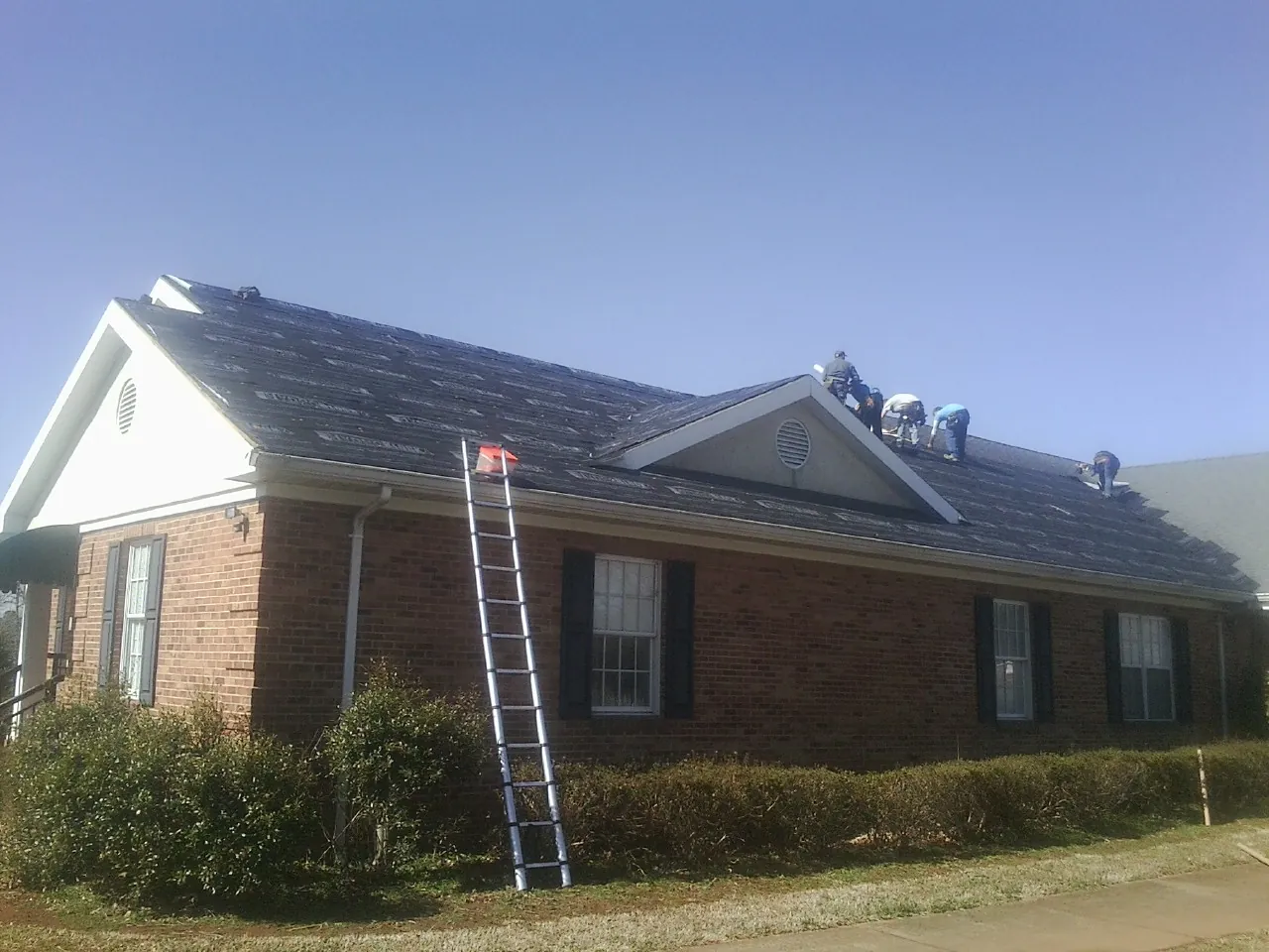 Crew tearing shingles off a brick ranch roof with a ladder set — Emergency Roof Repair work by our crew in Clarion