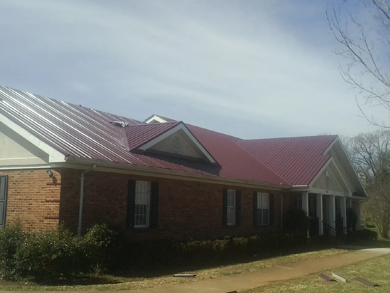 Red metal roof with gabled entries on a long brick building, from a Hail Damage Roof Repair job in Clarion