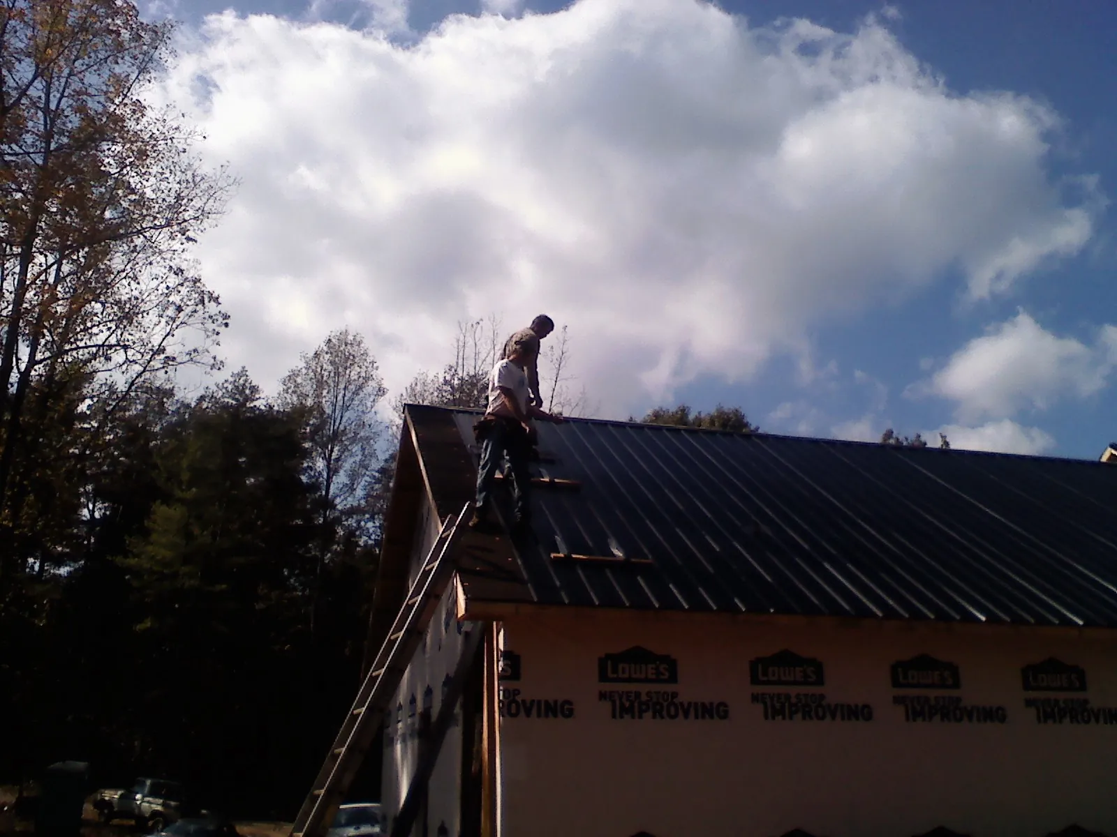 Roofer fastening dark metal panels high against a cloudy sky, from a Roof Inspection job in Clarion