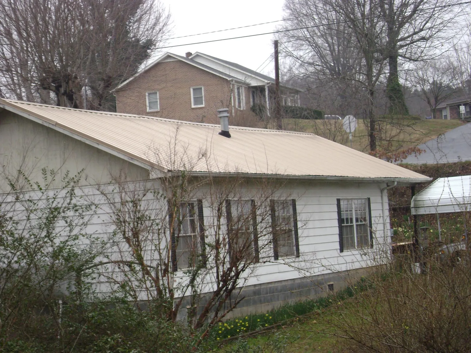Tan metal roof on a white sided house set into a hillside — Commercial Roofing by Roofing Brothers in Clarion