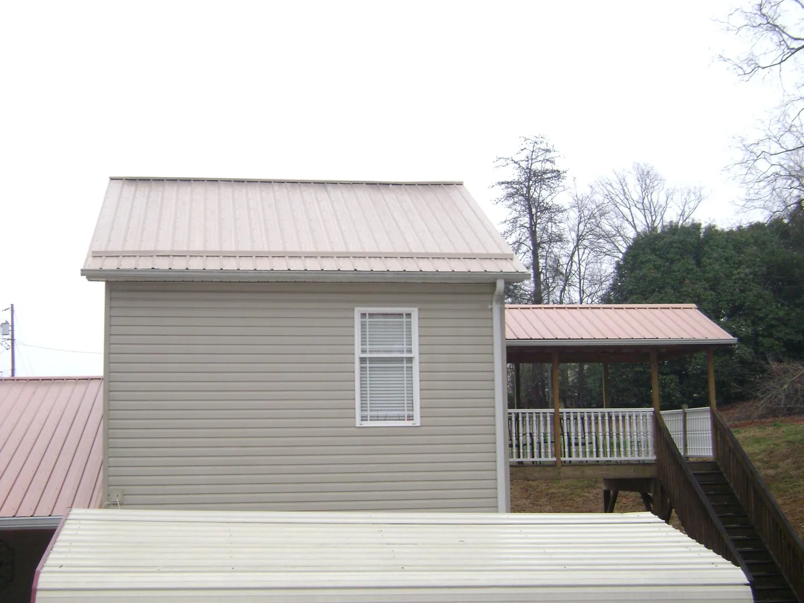 Tan metal roofs on a two story addition and attached porch, from a Roof Replacement job in Clarion